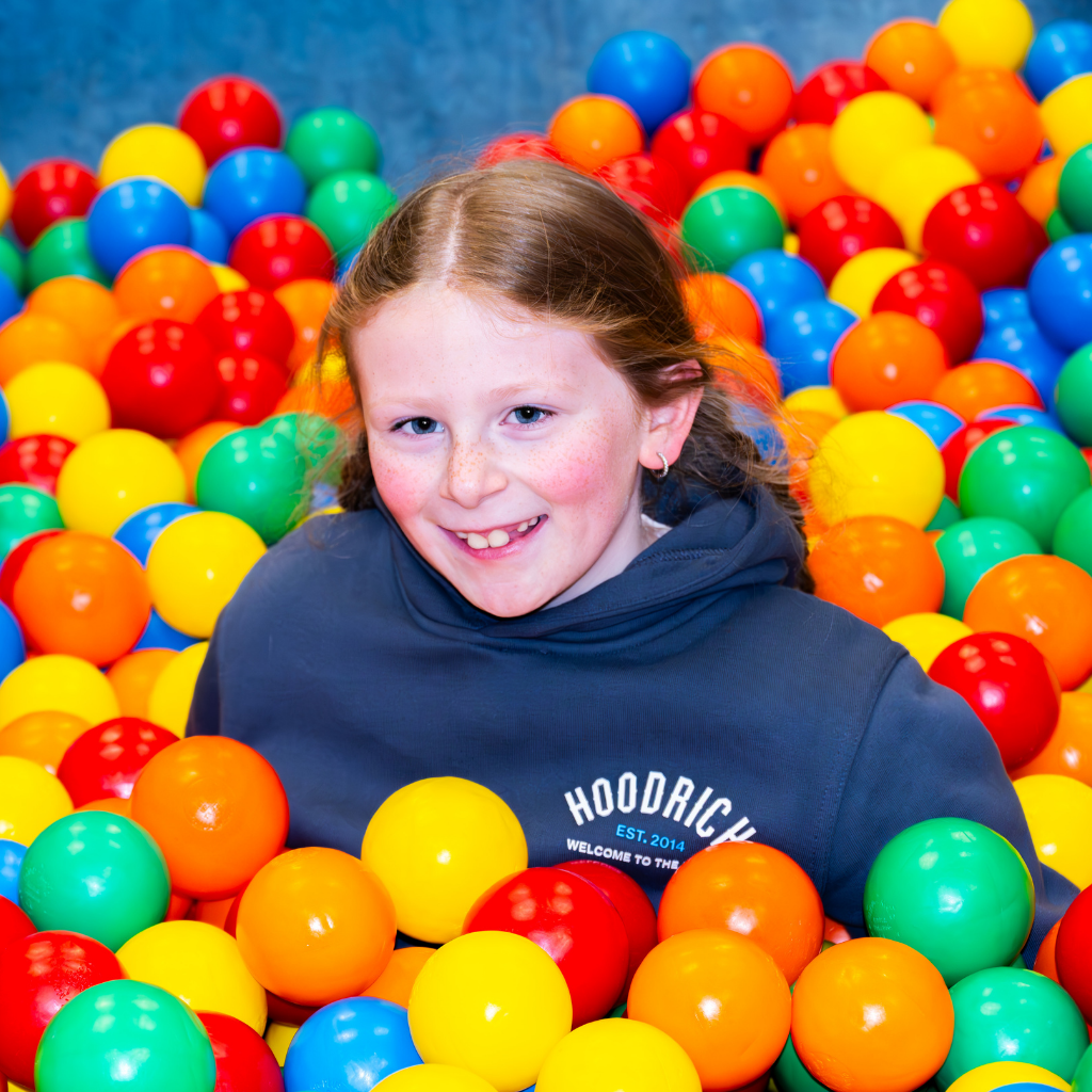 A child, smiling, in a ball pit of multicoloured balls